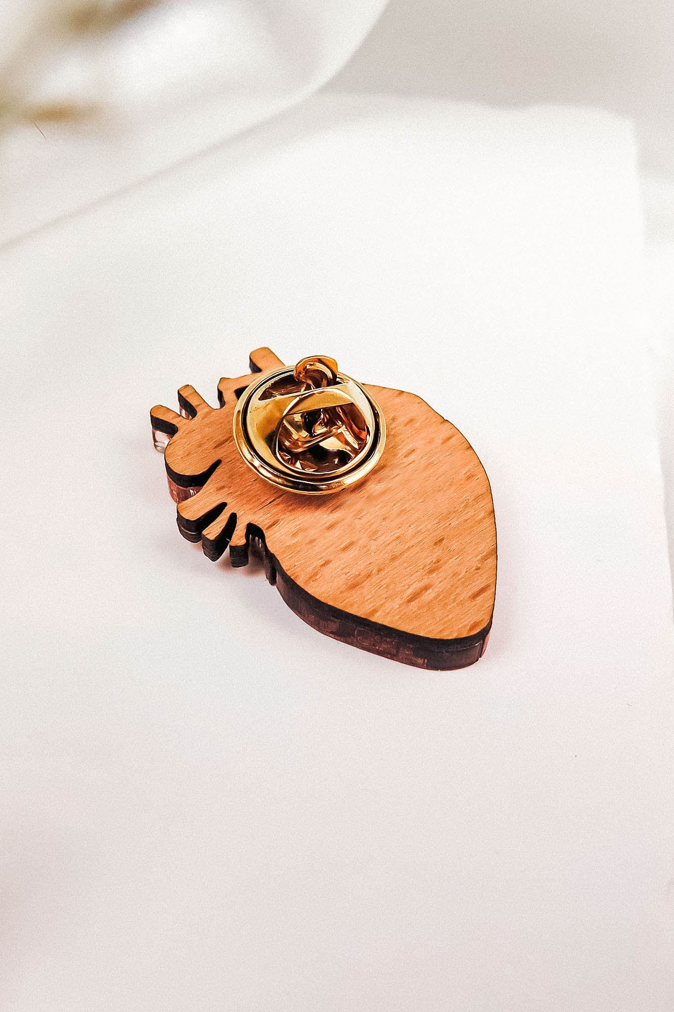 A unique, handcrafted wooden keychain shaped like an anatomical heart with a gold metal key ring attached, placed on a white surface with soft lighting.