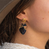 Close-up of a person wearing a gold and black Anatomical Heart Earring with gothic flair. The individual has light skin, brown hair, and is dressed in a beige hat and cream knitted sweater.