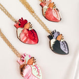 Four handcrafted jewelry necklaces with gold chains, each featuring an anatomical heart necklace pendant in dark red, pink, black and purple, or pink and mint green—making each one a unique jewelry piece displayed on a light background.