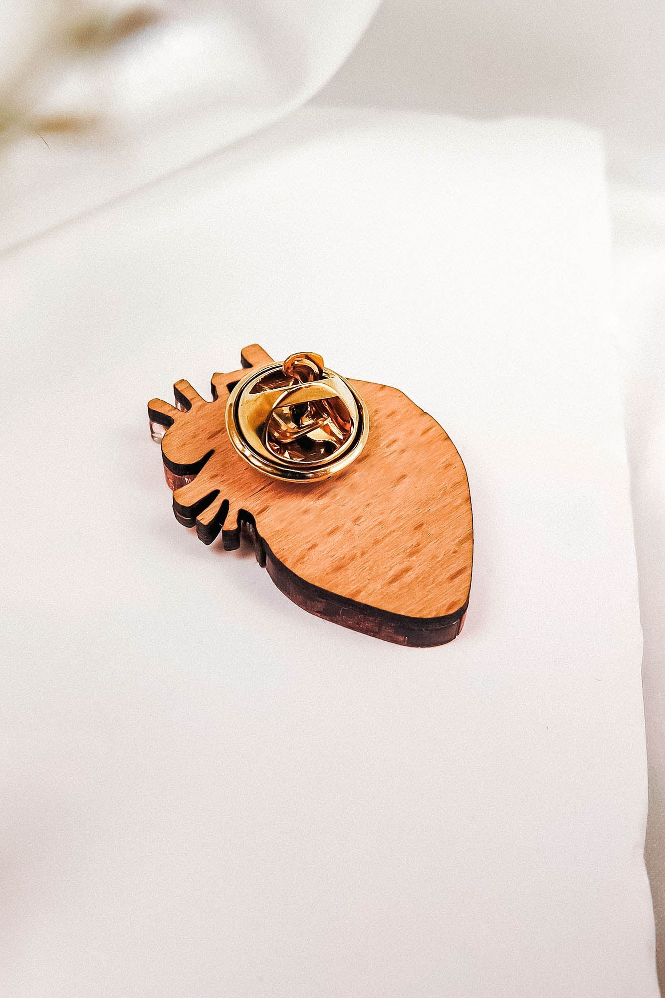 A handcrafted wooden keychain shaped like an anatomical heart with a gold metal key ring attached, resting on a white fabric background—a true statement piece for any collection.