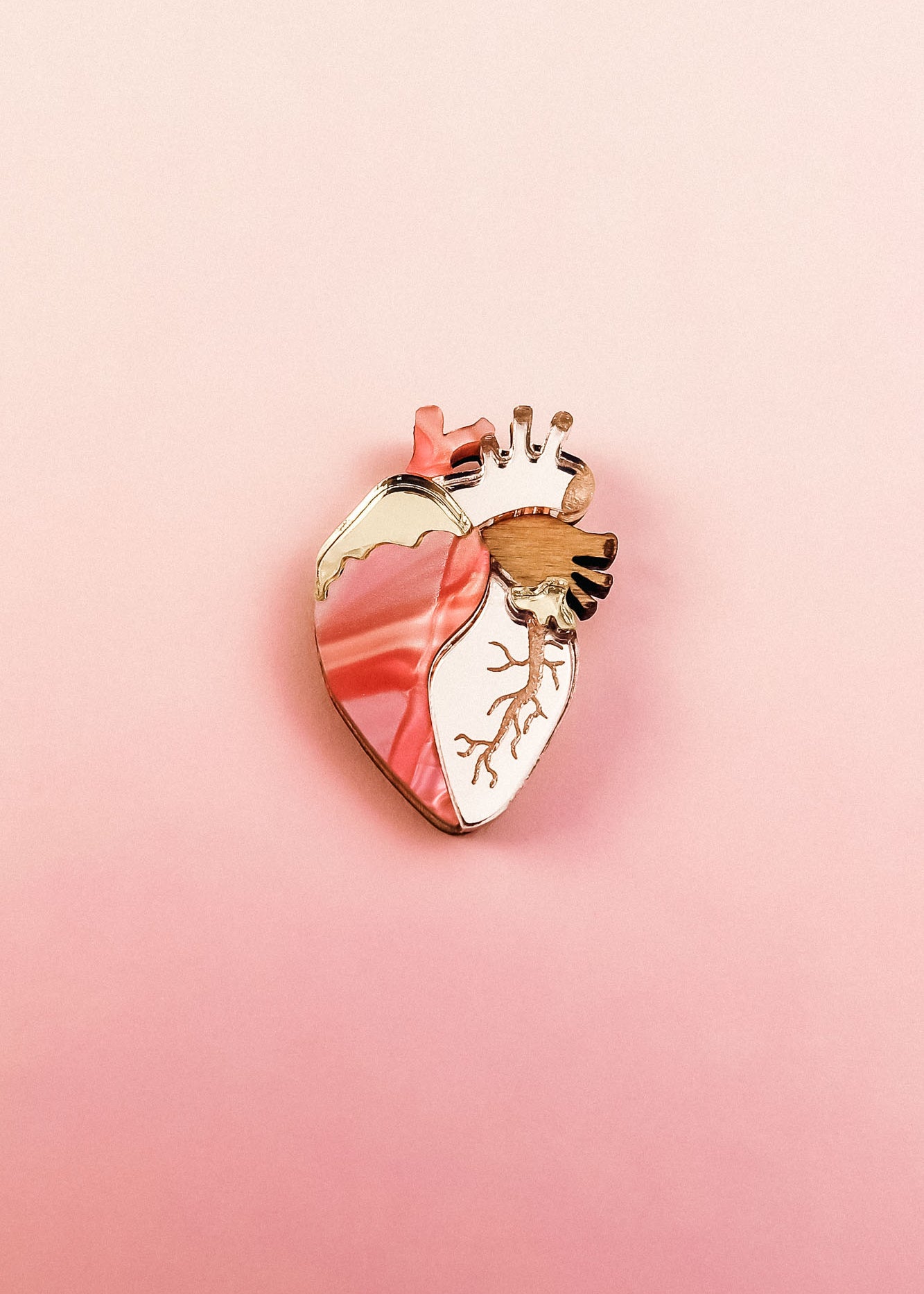 A unique, handcrafted Anatomical Heart Pin with gold accents is displayed on a pink gradient background, making it a striking decorative accessory.