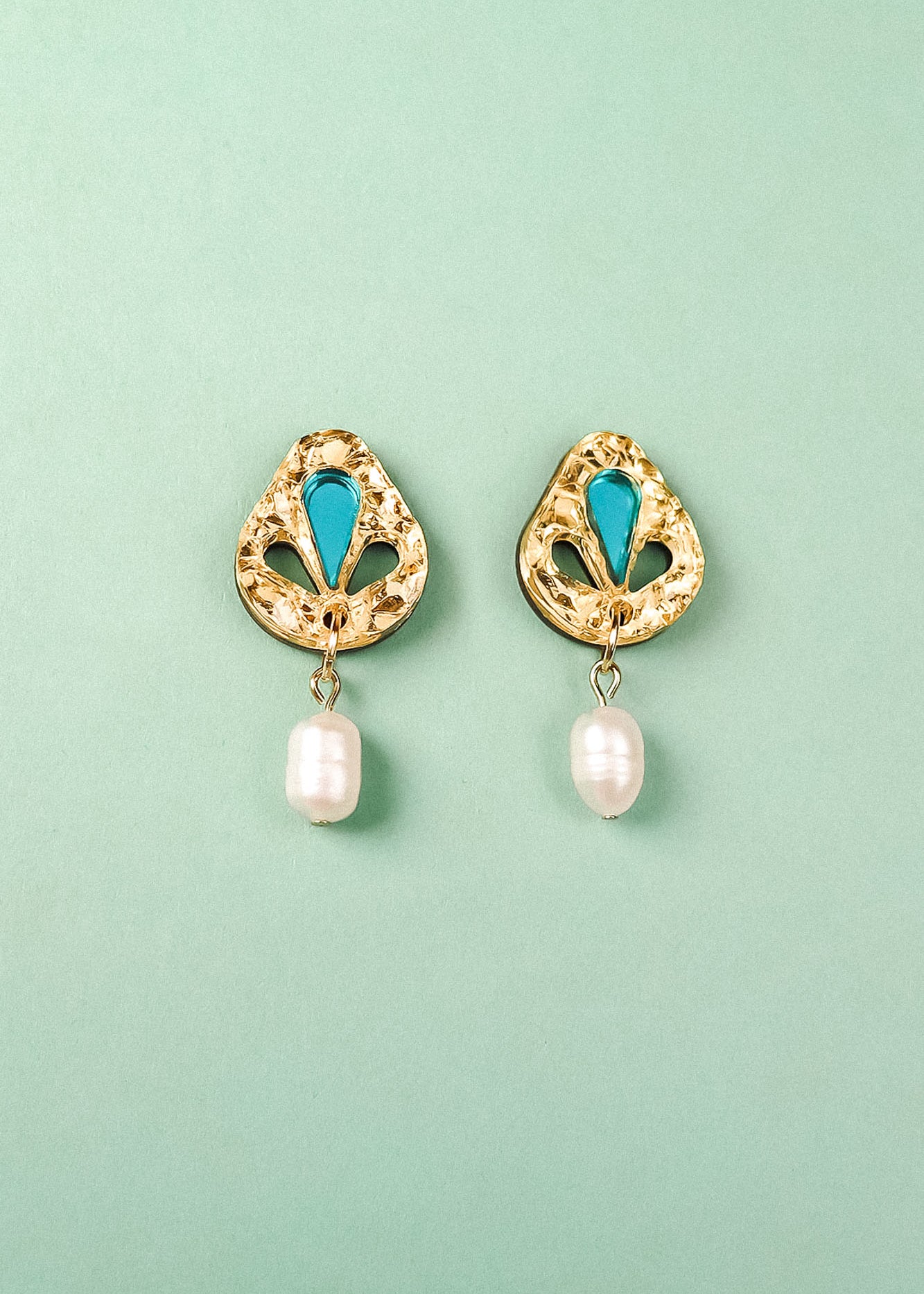 A pair of handcrafted gold-toned Basic Drop Earrings with turquoise accents and dangling white pearls, displayed on a light green background.