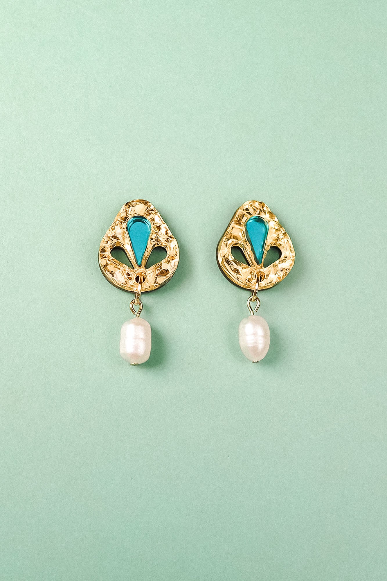 A pair of handcrafted gold-toned Basic Drop Earrings with turquoise accents and dangling white pearls, displayed on a light green background.
