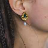 Close-up of a person’s ear wearing handcrafted Basic Drop Earrings featuring a gold setting with a green gemstone and dangling white pearl; the person has braided brown hair, perfect for minimalist fashion lovers.