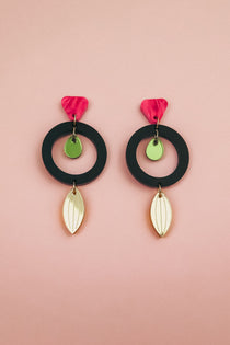 Pair of modern dangle earrings crafted from recycled acrylic, featuring black circular hoops, pink petal-shaped tops, small green discs, and gold leaf-shaped dangles, displayed on a soft pink background. Perfect artisan jewelry statement.