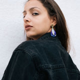 Woman with long brown hair wears a black denim jacket and handcrafted Crocus Flower Earrings, looking over her shoulder against a plain, light-colored background.