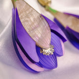 Close-up of handcrafted Crocus Flower Earrings, a statement accessory shaped like purple blossoms with layered petals and a translucent, textured center, resting on a white fabric background.