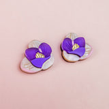 Crocus Stud Earrings shaped like purple flowers with yellow centers, set against a light pink background. The petals are layered, hand-painted flowers with a delicate, handmade appearance and are allergy-free.