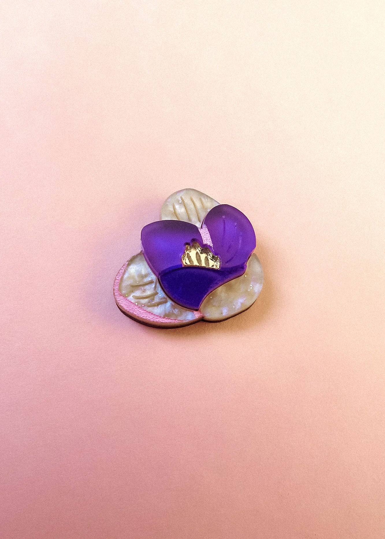 A handcrafted Purple Crocus Flower Lapel Pin, this decorative brooch features pearly cream petals and a translucent purple petal, perfect for nature lovers, set against a soft pink gradient background.