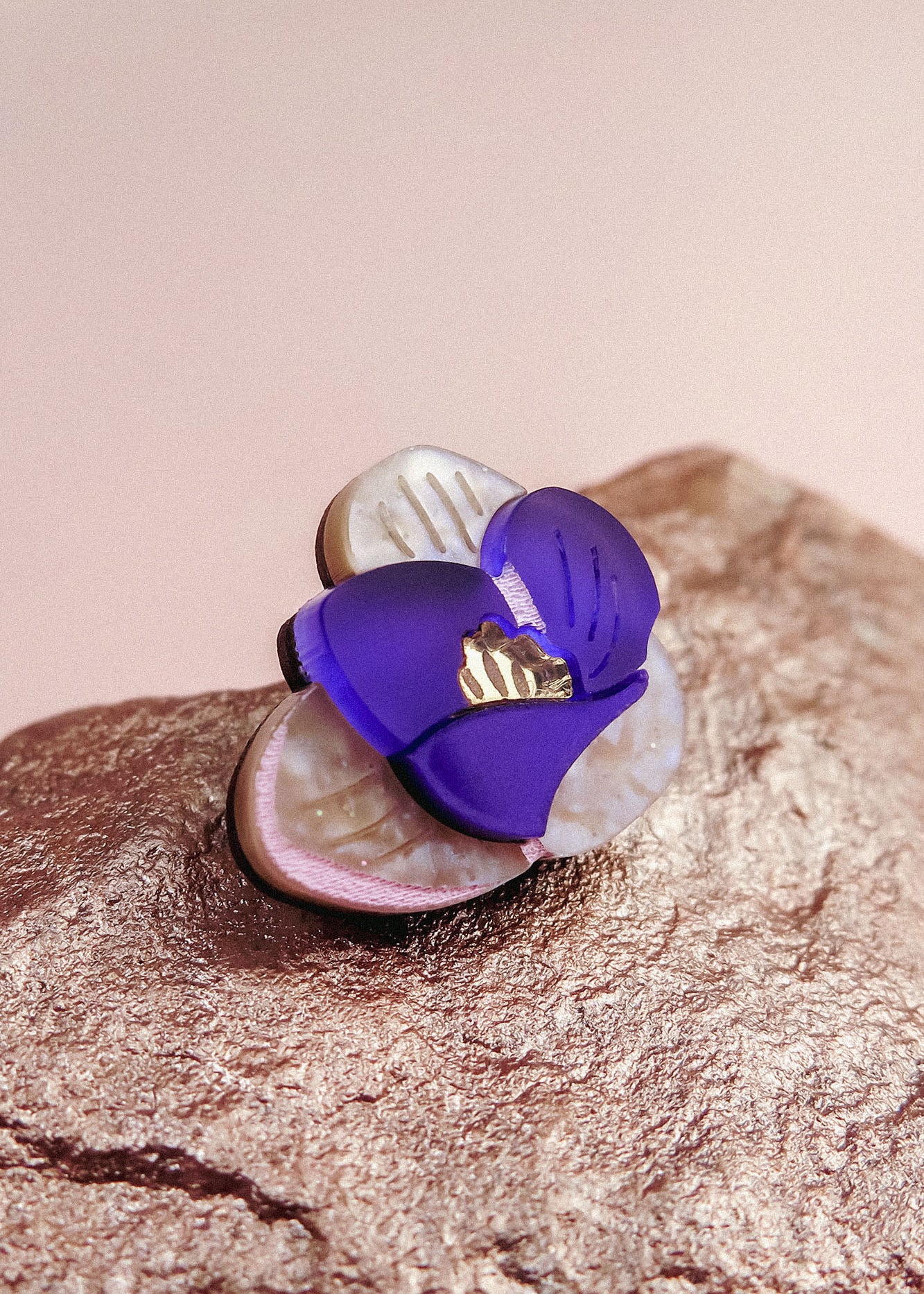 A close-up of a handcrafted Purple Crocus Flower Lapel Pin with purple and white petals and a gold center, resting on a textured, metallic-looking surface—perfect for nature lovers.