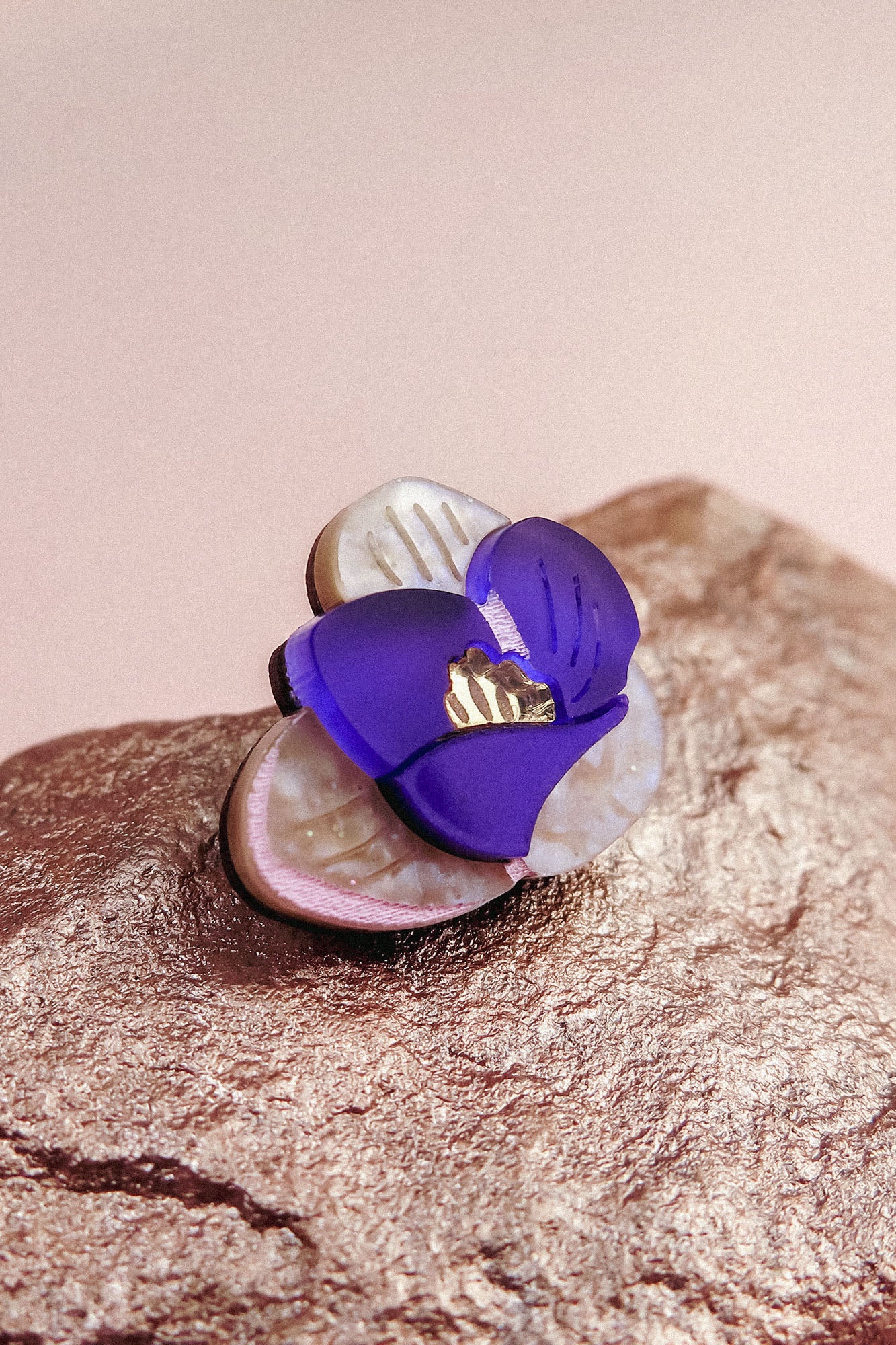A close-up of a handcrafted Purple Crocus Flower Lapel Pin with purple and white petals and a gold center, resting on a textured, metallic-looking surface—perfect for nature lovers.