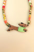 A colorful, handcrafted Dachshund necklace featuring a patterned cord and a pendant shaped like a brown dachshund in a green sweater, made from recycled materials and shown against a beige background.