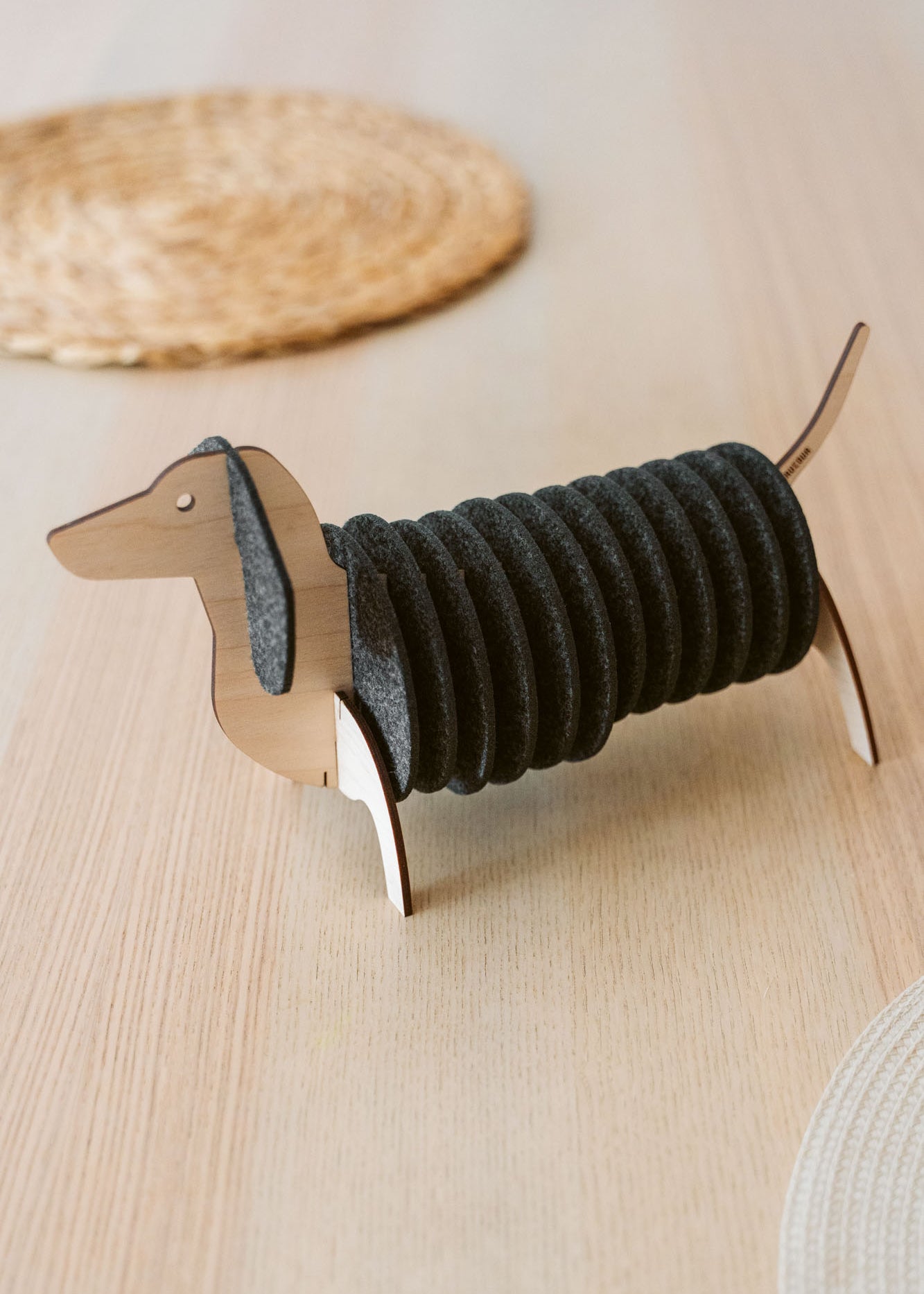 A napkin holder shaped like a dachshund dog, made of wood with black felt napkins forming the dog's body, sits on a light wooden table—perfect for pairing with matching felt coasters or Dachshund coasters for a charming tablescape.