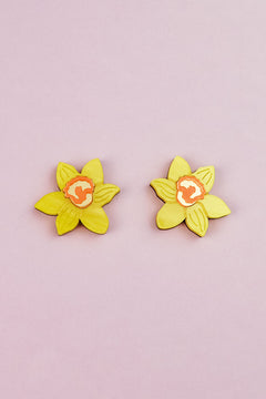 Two yellow Daffodil Stud Earrings with orange centers, resembling, are arranged side by side on a light pink background—perfect for stylish women seeking unique accessories.