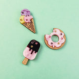 Three handcrafted clay pins on a mint green background: an ice cream cone, a Donut Pin with colorful rhinestones and sprinkles, and a pink-and-black popsicle.