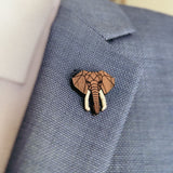 A close-up of a person wearing a light blue suit jacket with a handcrafted Elephant Pin attached to the lapel. The pin showcases a geometric design, highlighting the elephant’s trunk and tusks.