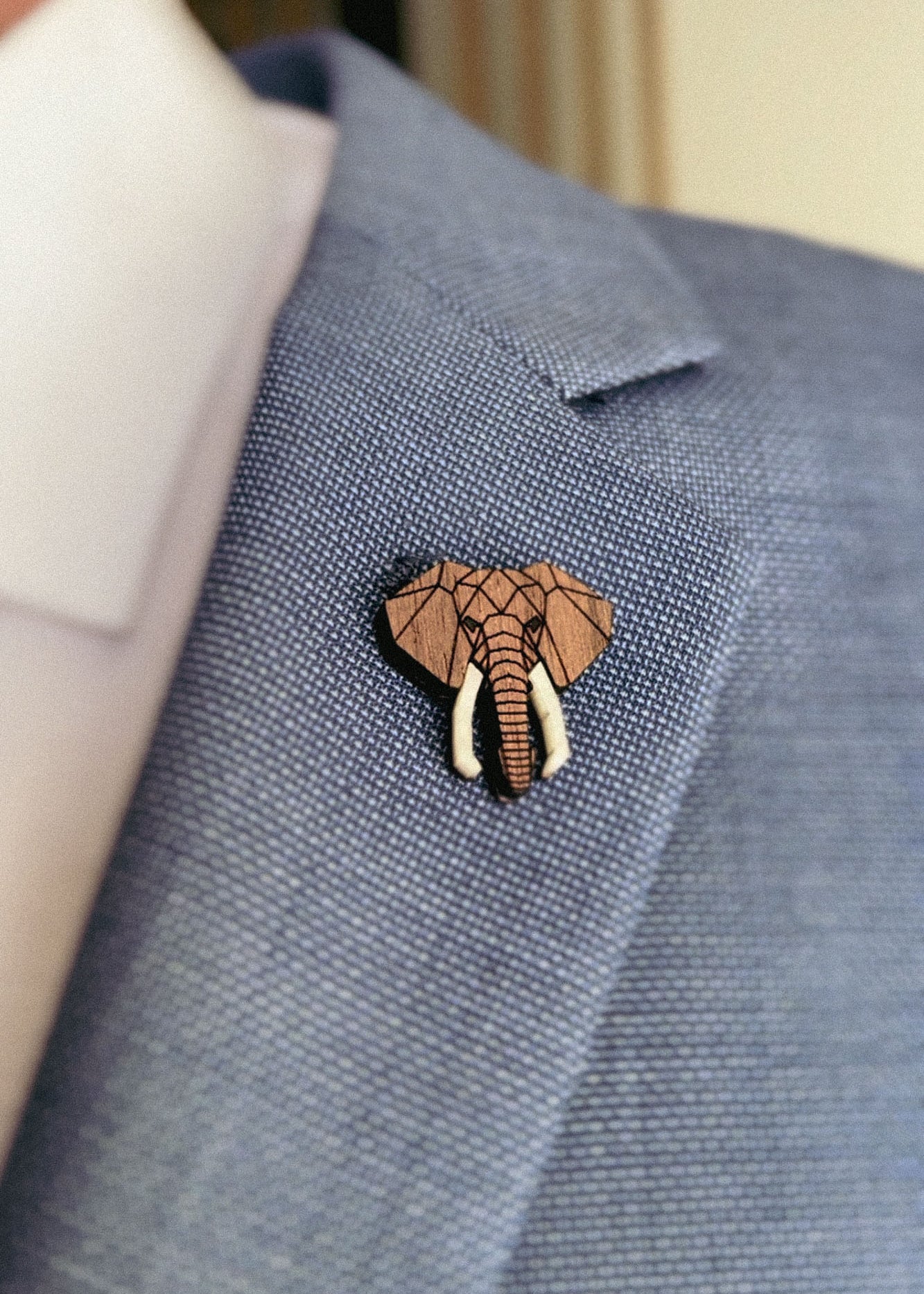 A close-up of a person wearing a light blue suit jacket with a handcrafted Elephant Pin attached to the lapel. The pin showcases a geometric design, highlighting the elephant’s trunk and tusks.