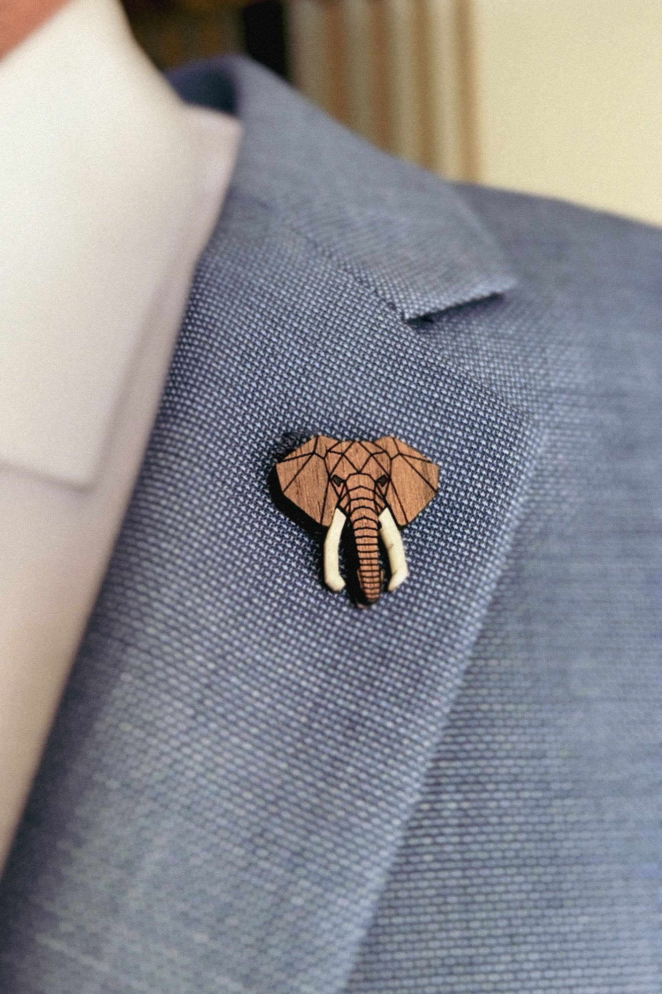 A close-up of a person wearing a light blue suit jacket with a handcrafted Elephant Pin attached to the lapel. The pin showcases a geometric design, highlighting the elephant’s trunk and tusks.