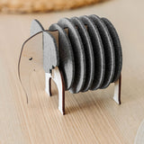 A set of round, gray Elephant Coasters is stacked vertically in a wooden holder shaped like an elephant, adding witty design and furniture protection to your light wood table.