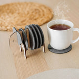 A set of round Elephant Coasters with witty design sits in a wooden elephant-shaped holder on a table, offering furniture protection while a white mug rests on one coaster.