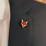 A close-up of a dark suit jacket with a handcrafted fox pin made from recycled wood, plus a hint of white dress shirt and patterned pocket square—an eco-conscious accessory for the modern gentleman.