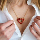 A close-up of a person in a white shirt, holding the collar open to reveal a handcrafted gold necklace with a geometric red heart pendant—an elegant Fragment of Love Necklace displayed around their neck.