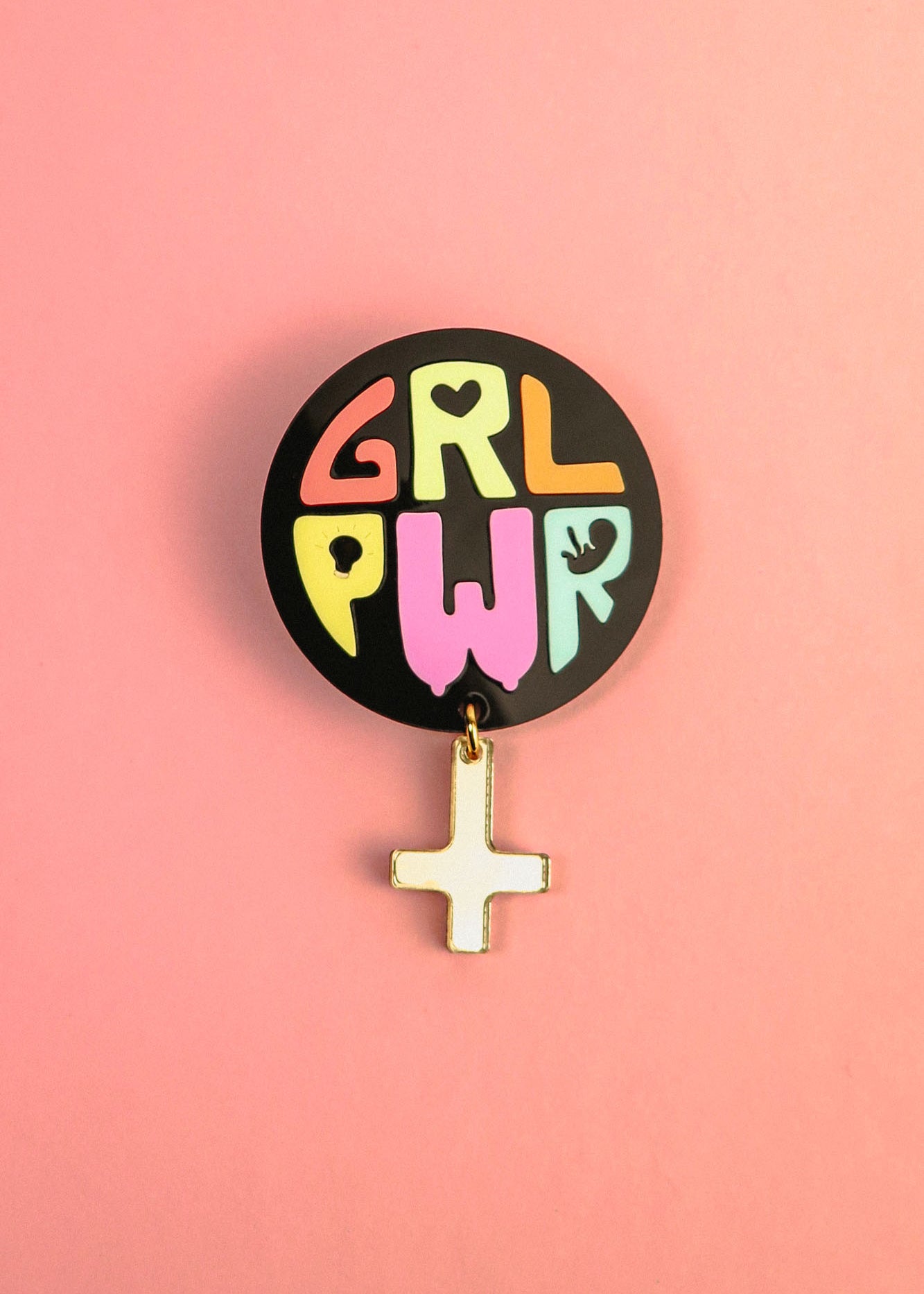 A round black pin with colorful letters spelling GRL PWR and a dangling gold Venus symbol, this handcrafted accessory celebrates meaningful symbolism, set against a vibrant pink background.