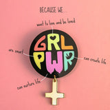 A colorful Girl Power Brooch reading GRL PWR is pinned to a pink background. Text around it says: Because we... want to love and be loved, are smart, can nurture life, can create life, with lines pointing to the badge.