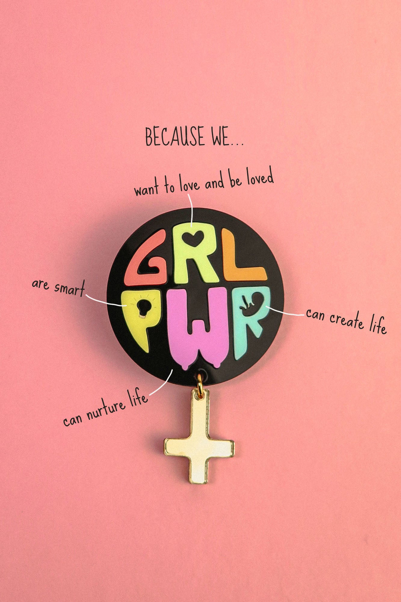 A colorful Girl Power Brooch reading GRL PWR is pinned to a pink background. Text around it says: Because we... want to love and be loved, are smart, can nurture life, can create life, with lines pointing to the badge.