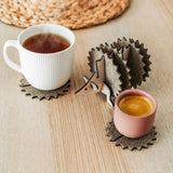 A white mug and a pink cup sit on spiky felt coasters shaped like a hedgehog, adding playful home decor flair to a light wooden table with a woven placemat in the background.