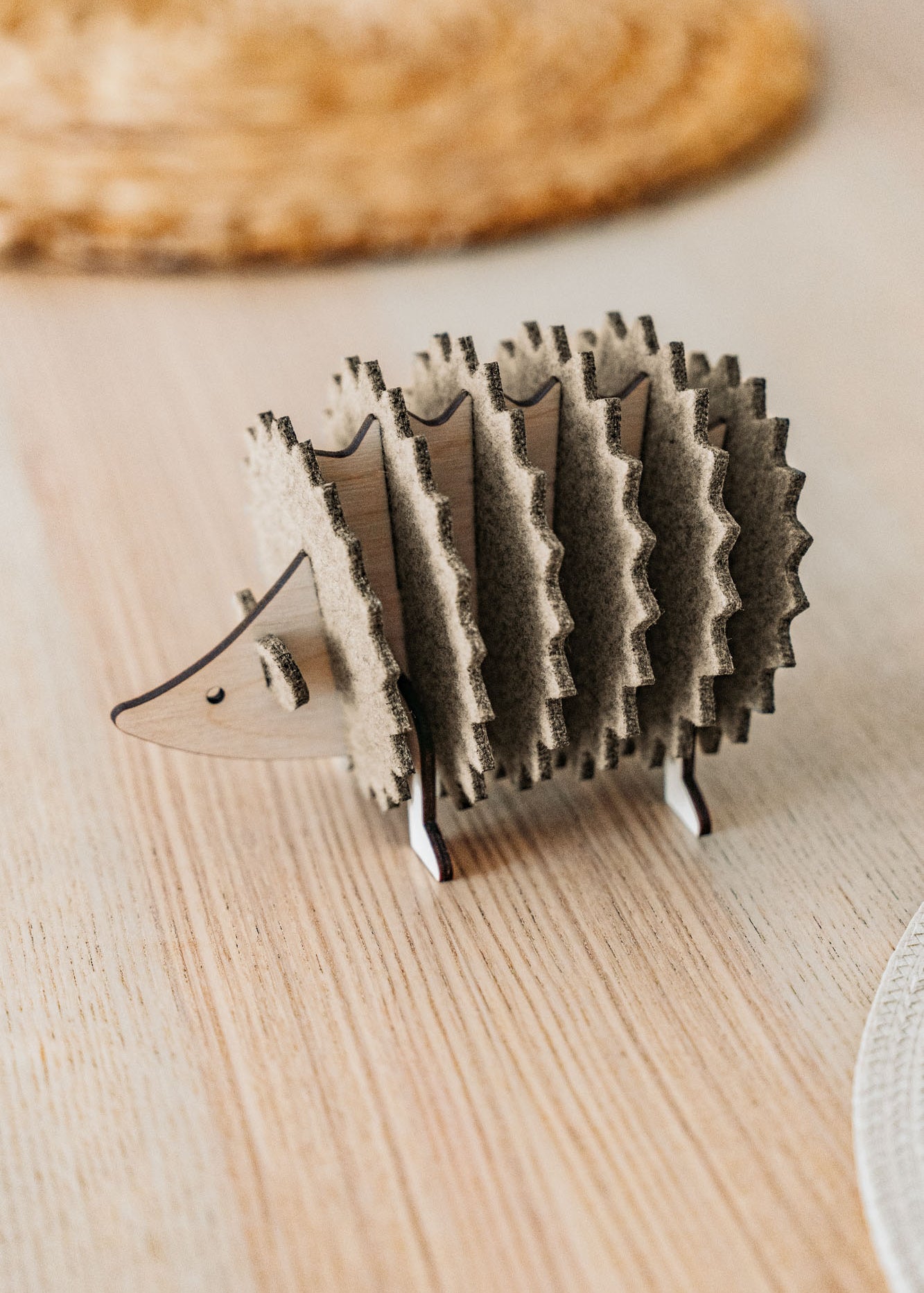 A small, wooden hedgehog-shaped coaster holder made of wood and felt sits on a light wooden table with a woven placemat in the background, adding a charming touch to your home decor.