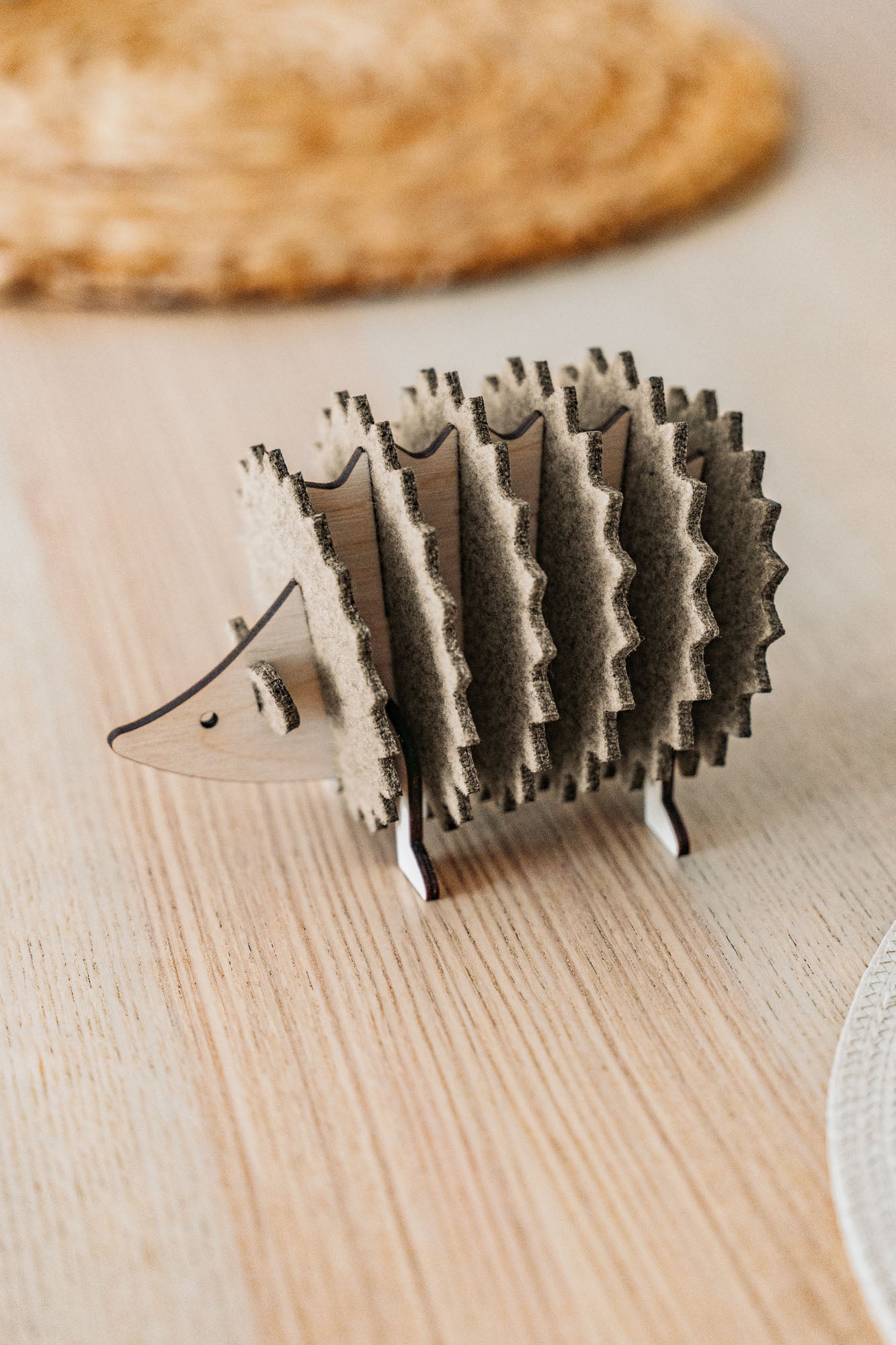 A small, wooden hedgehog-shaped coaster holder made of wood and felt sits on a light wooden table with a woven placemat in the background, adding a charming touch to your home decor.
