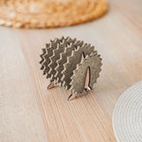 A small, decorative wooden hedgehog coaster holder made of felt and plywood sits on a wooden table, adding charm to your home decor, with woven placemats in the background.