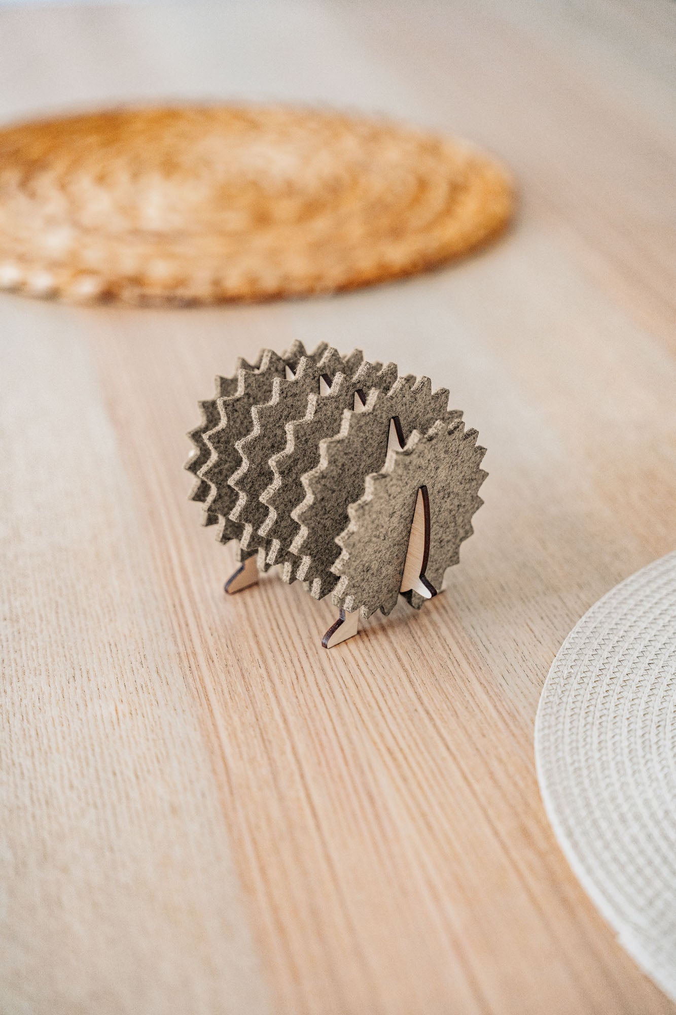 A small, decorative wooden hedgehog coaster holder made of felt and plywood sits on a wooden table, adding charm to your home decor, with woven placemats in the background.