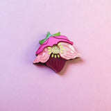 A colorful enamel lapel pin shaped like a strawberry with pink petals and green leaves is displayed on a soft pink background—perfect for handmade accessory lovers or fans of the unique purple hellebore flower.