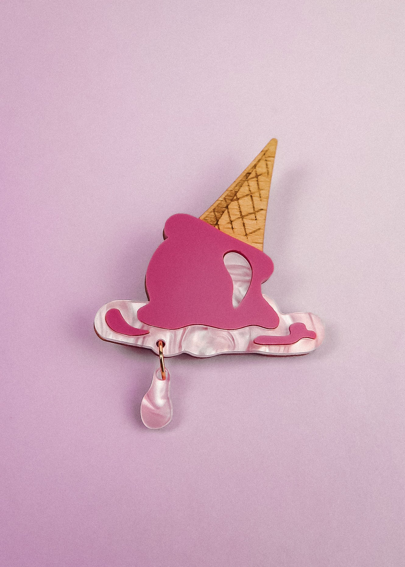 A handcrafted Melted Ice Cream Brooch shaped like a melting cone, with a pink scoop, tan cone, and teardrop charm, set against a light purple background—perfect for adding sweet whimsy to your summer wardrobe.