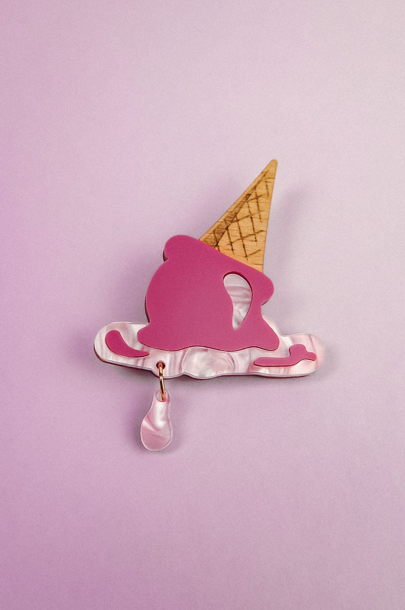 A handcrafted Melted Ice Cream Brooch shaped like a melting cone, with a pink scoop, tan cone, and teardrop charm, set against a light purple background—perfect for adding sweet whimsy to your summer wardrobe.