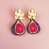 Handcrafted Fig Earrings featuring gold mirror leaves, purple outer edges, and bright pink centers, beautifully displayed on a light pink background.