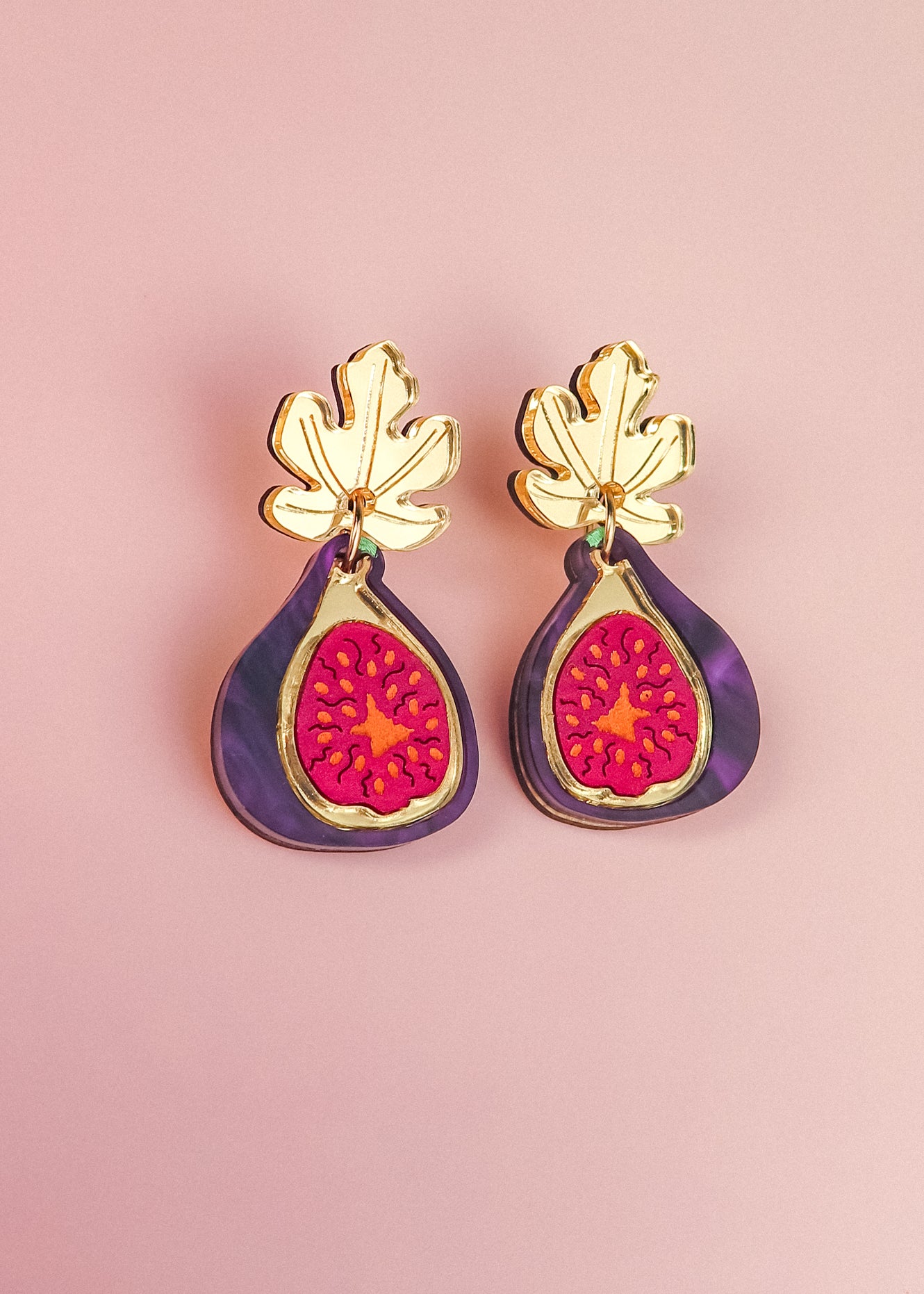 Handcrafted Fig Earrings featuring gold mirror leaves, purple outer edges, and bright pink centers, beautifully displayed on a light pink background.