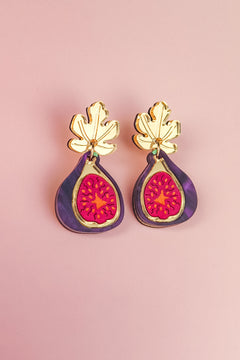 Handcrafted Fig Earrings featuring gold mirror leaves, purple outer edges, and bright pink centers, beautifully displayed on a light pink background.