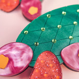 Brightly colored, stylized opuncia cactus artwork featuring a green pad with a diamond pattern and small gems, surrounded by pink and orange glittery and marbled pads—this bold design pops against a soft pink background.