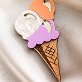 A handcrafted Ice Cream Brooch featuring three scoops—white, orange, and purple—on a wooden cone, displayed on smooth, light-colored satin fabric. Perfect for adding a playful touch to your summer look.