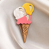 A handcrafted accessory, this Ice Cream Brooch features a wooden cone with yellow, white, and pink scoops, resting on smooth cream-colored satin—perfect for adding charm to your summer look.