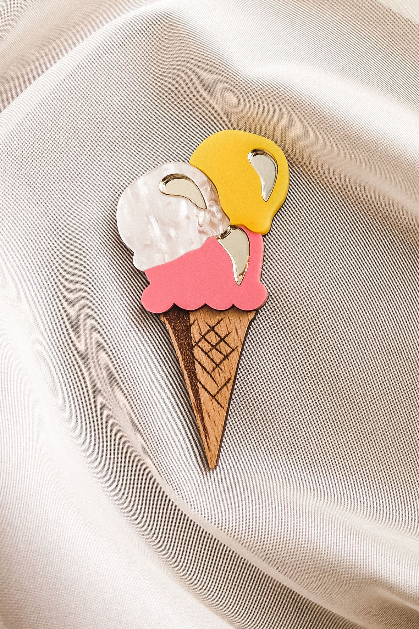 A handcrafted accessory, this Ice Cream Brooch features a wooden cone with yellow, white, and pink scoops, resting on smooth cream-colored satin—perfect for adding charm to your summer look.