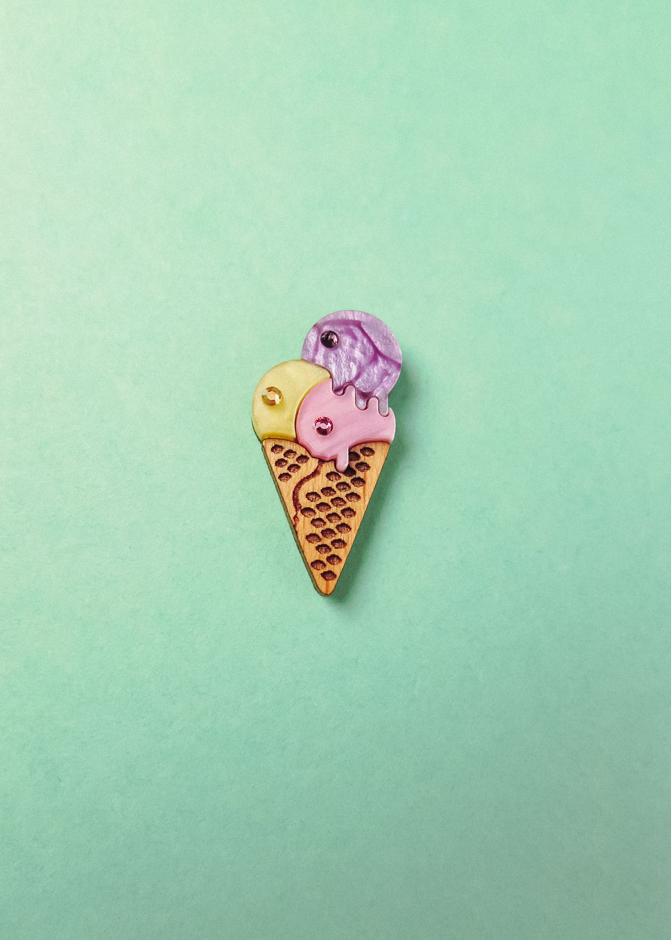 A handcrafted Ice Cream Pin with a playful design features three whimsical scoops—yellow, pink, and purple—on a light green background.