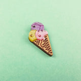 A small, handcrafted Ice Cream Pin with a playful design featuring yellow, purple, and pink scoops topped with gemstone accents, set against a pastel green background.