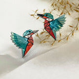 Eco-friendly Kingfisher Stud Earrings: Two colorful origami-style bird earrings with turquoise wings and red bodies, placed on a white textured surface with delicate dried grass in the background.