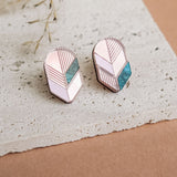 A pair of geometric stud earrings with pink, white, and teal segments set in silver, displayed on a textured white stone surface with dried grass in the background—perfect for lovers of minimalist jewelry.