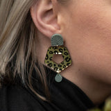 Close-up of a person with light blond hair wearing Leopard Earrings crafted from premium materials, featuring a leopard print hexagonal shape with green and gold accents for an eye-catching look.
