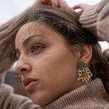 A woman in a brown turtleneck sweater gazes thoughtfully to the side, hands raised behind her head. She wears Leopard Earrings made from premium materials, their timeless patterns adding bold elegance to her look.